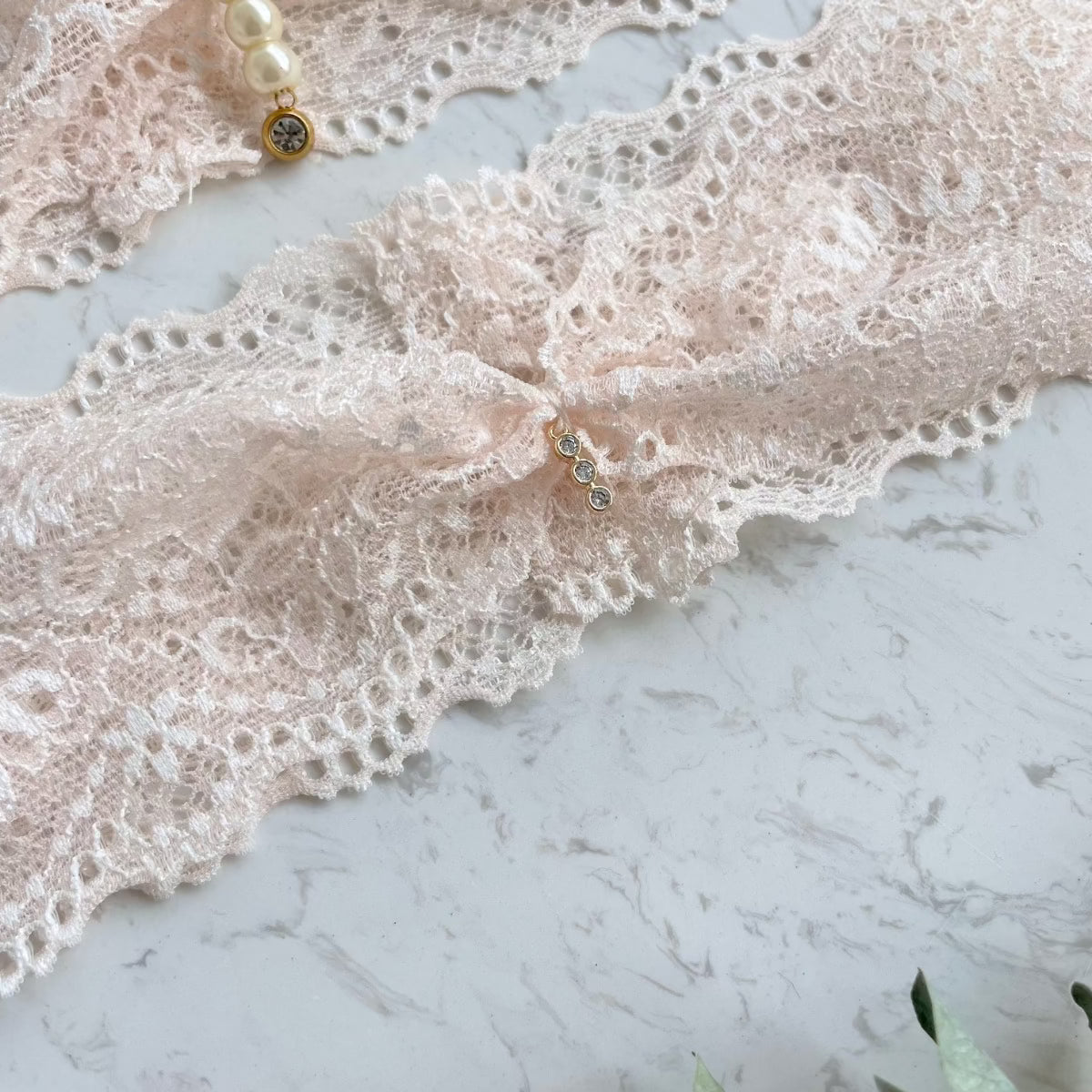 Detailansicht des Anhängers an einem Strumpfband aus zarter blush Spitze.
