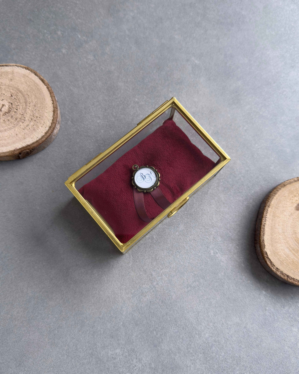 Geschlossenes Ringkästchen aus Glas mit goldenem Rahmen, rotem Ringkissen und personalisiertem Anhänger in der Draufsicht.