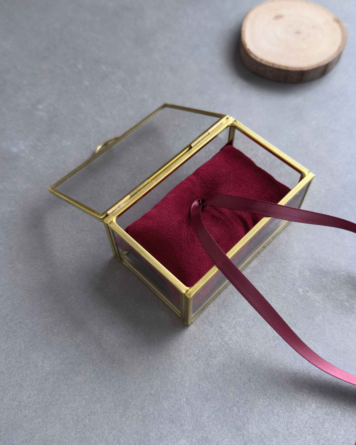Offenes Ringkästchen mit goldenem Rahmen und rotem Ringkissen mit Satinband in schräger Ansicht.