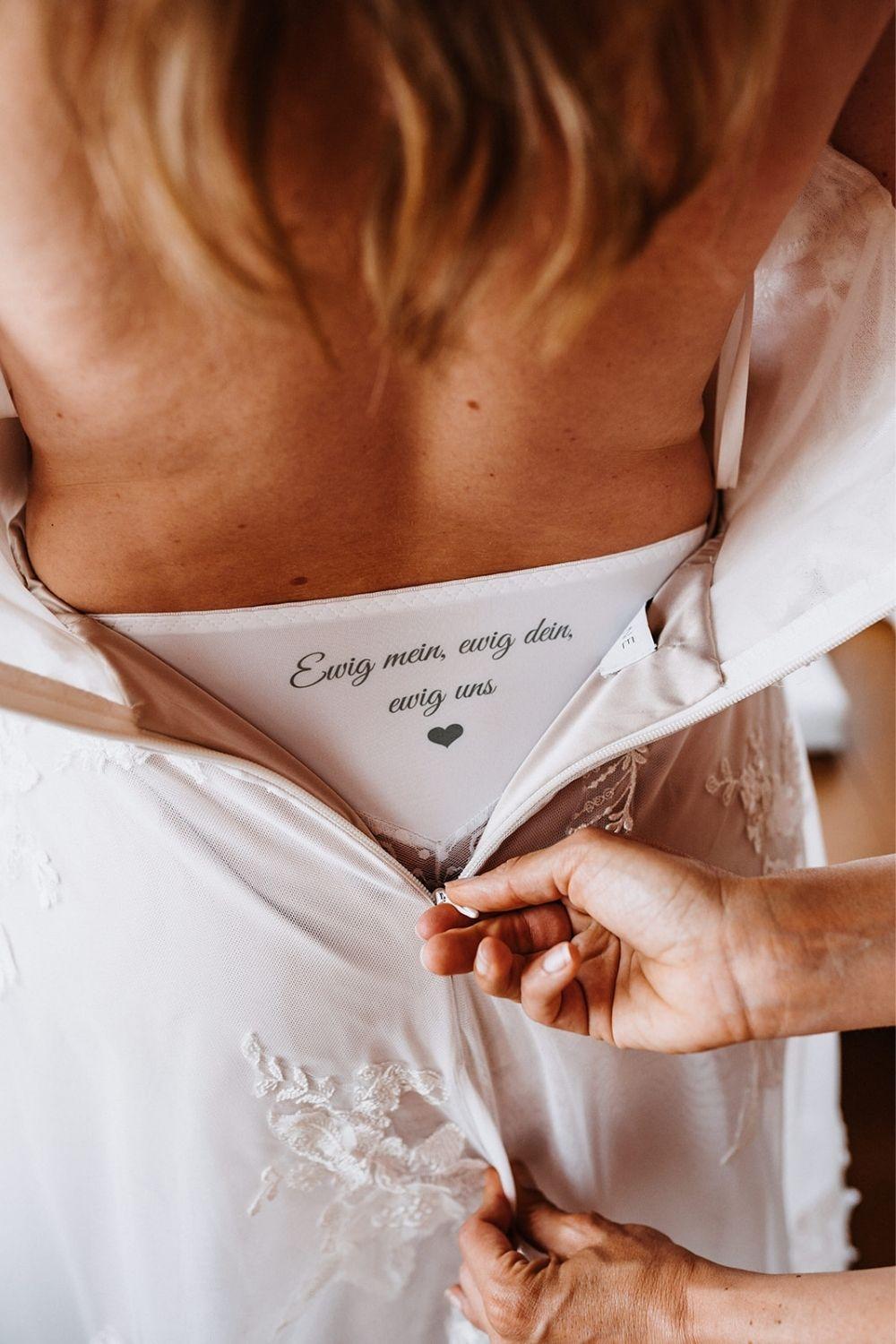 Personalisierter Braut-Slip mit individuellem Text „Ewig mein, ewig dein, ewig uns“ und Herz-Motiv; Rückansicht einer Braut im Hochzeitskleid, das den Aufdruck der Unterwäsche am Rücken enthüllt.