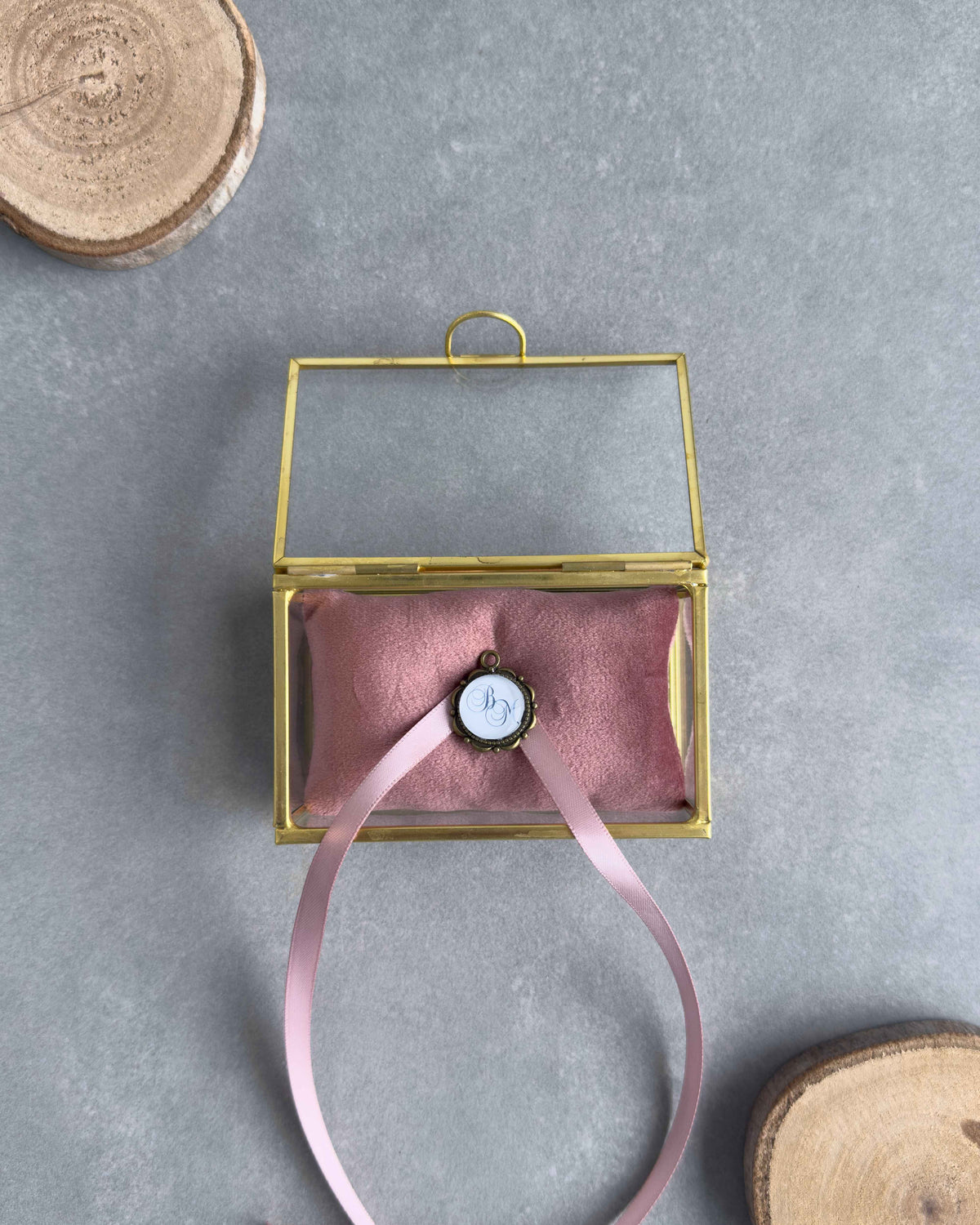 Offenes Ringkästchen aus Glas mit altrosafarbenem Ringkissen und personalisiertem Anhänger mit Initialen in der Frontansicht.