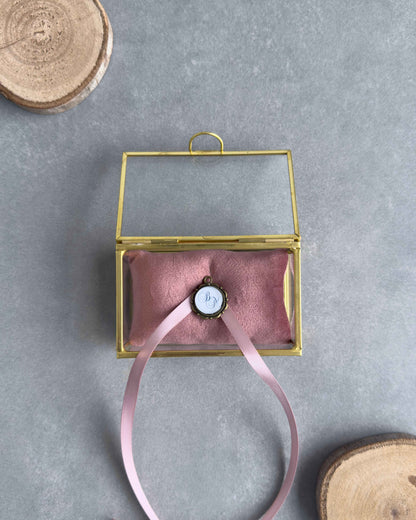 Offenes Ringkästchen aus Glas mit altrosafarbenem Ringkissen und personalisiertem Anhänger mit Initialen in der Frontansicht.