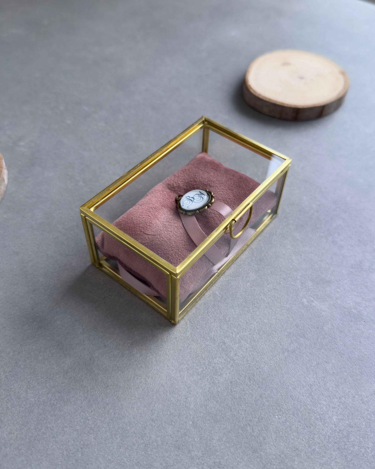 Geschlossenes Ringkästchen aus Glas mit Ringkissen in Altrosa und personalisiertem Anhänger mit Initialen in seitlicher Ansicht.