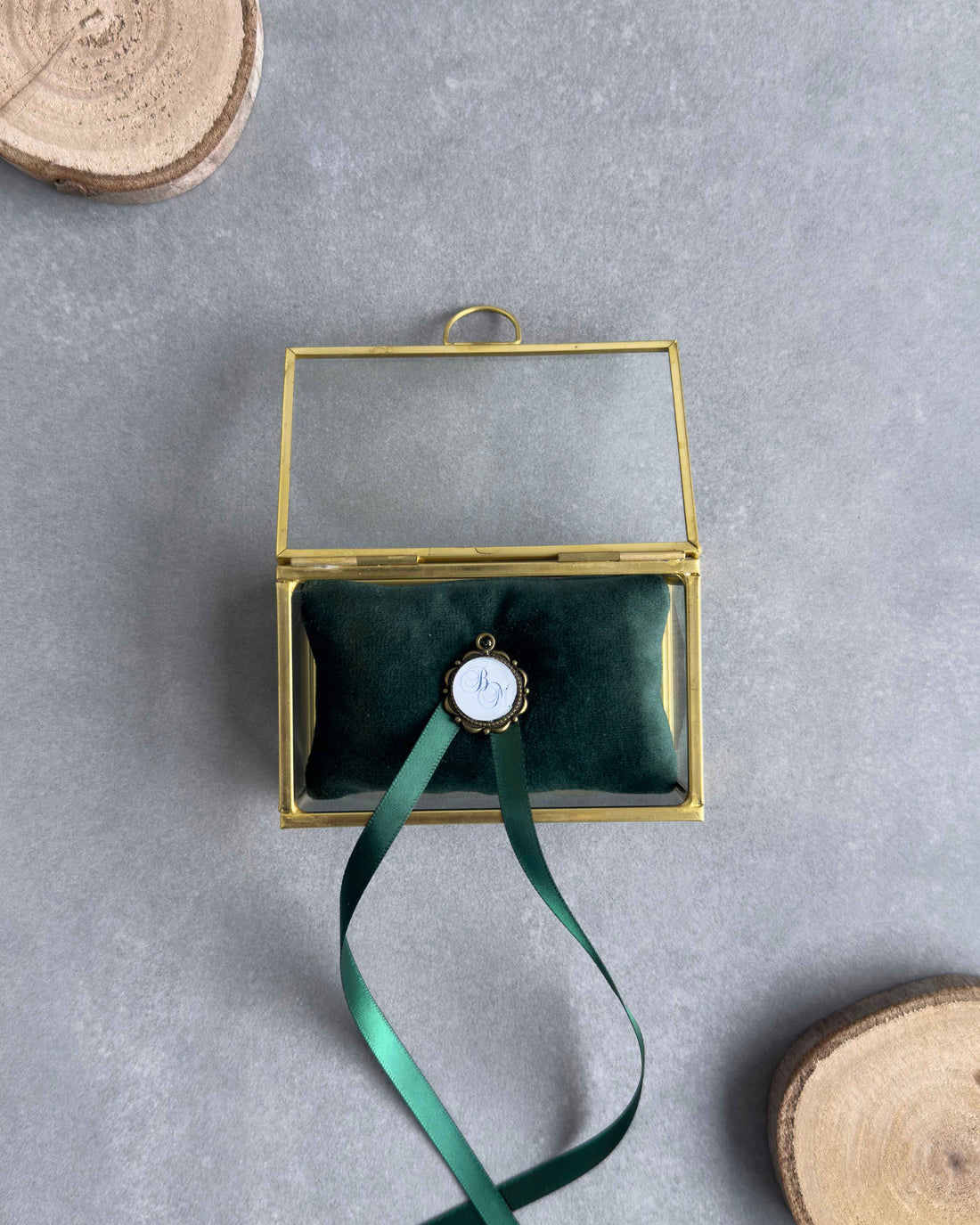 Offenes Ringkästchen aus Glas in Gold mit grünem Ringkissen und personalisiertem Anhänger in Frontansicht.