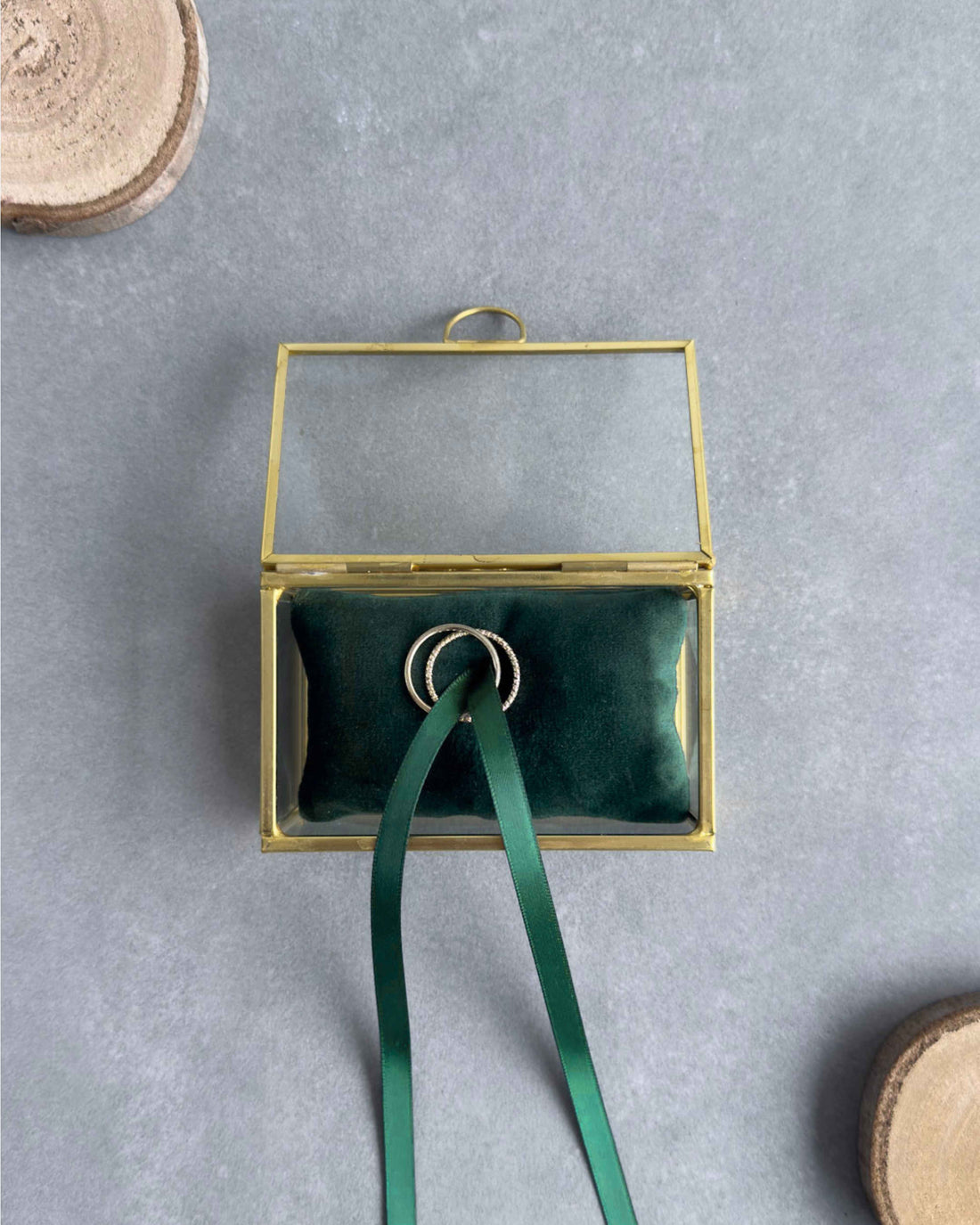 Offenes Ringkästchen aus Glas in Gold mit grünem Ringkissen und Eheringen in Frontansicht.