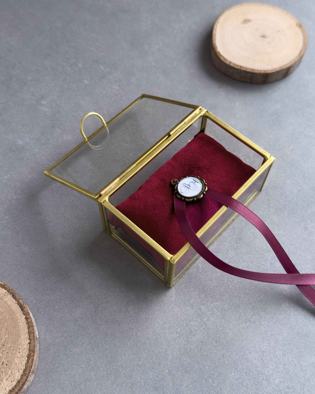 Offenes Ringkästchen aus Glas mit rotem Ringkissen und personalisiertem Anhänger in schräger Ansicht.