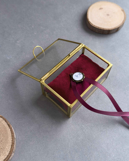 Offenes Ringkästchen aus Glas mit rotem Ringkissen und personalisiertem Anhänger in schräger Ansicht.