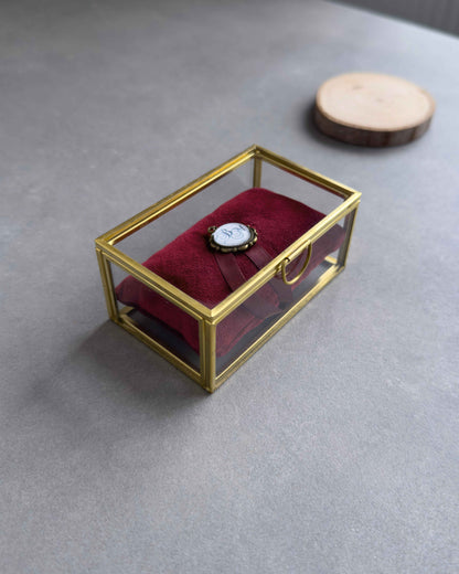 Geschlossenes Ringkästchen aus Glas mit rotem Ringkissen und personalisiertem Anhänger in seitlicher Ansicht.