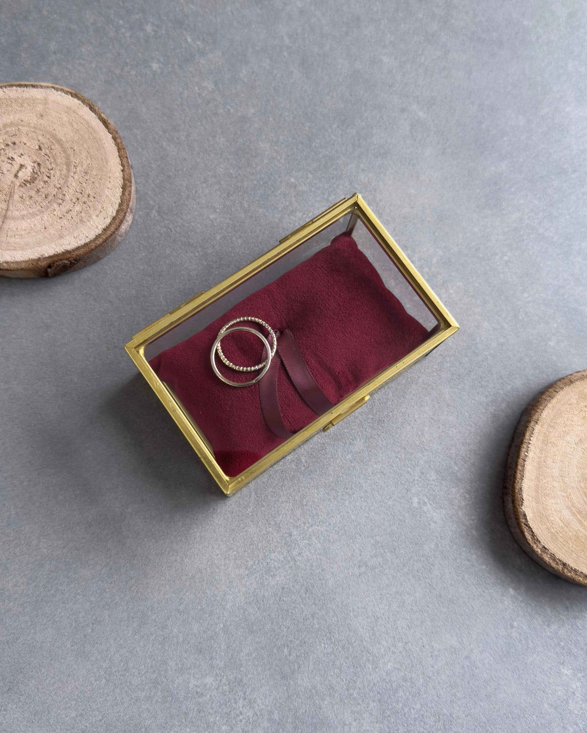 Geschlossenes Ringkästchen aus Glas mit rotem Ringkissen und zwei Eheringen, von oben fotografiert.